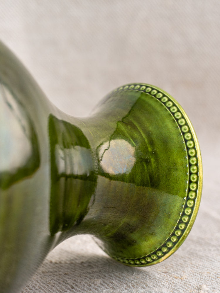 Base of mid-century French Pichon Uzès vase in glossy green earthenware with beaded border on beige textured surface.