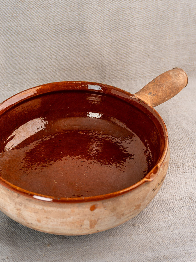 Vintage French Vallauris poêlon by Ste Commerciale, round terracotta pan with glossy brown interior on gray fabric.