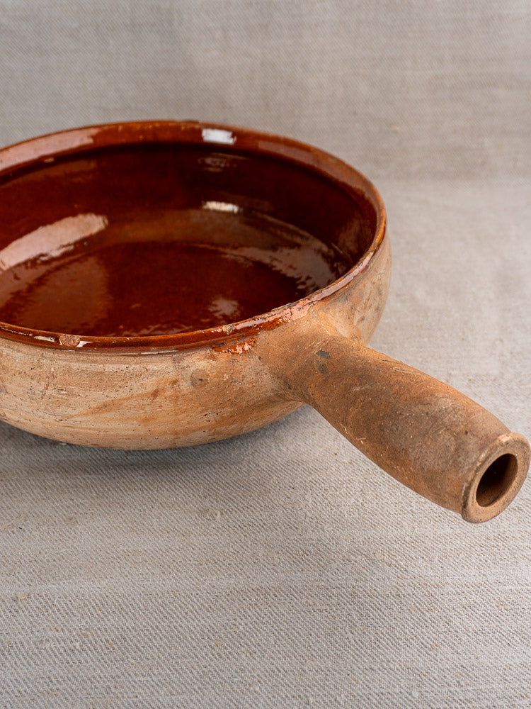 Vintage French Vallauris terracotta poêlon with single thick handle on light gray fabric.