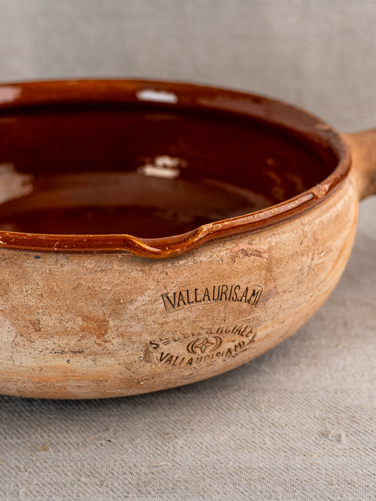 Vintage French Vallauris ceramic cooking pan with handle, brown glazed interior, on beige fabric background.