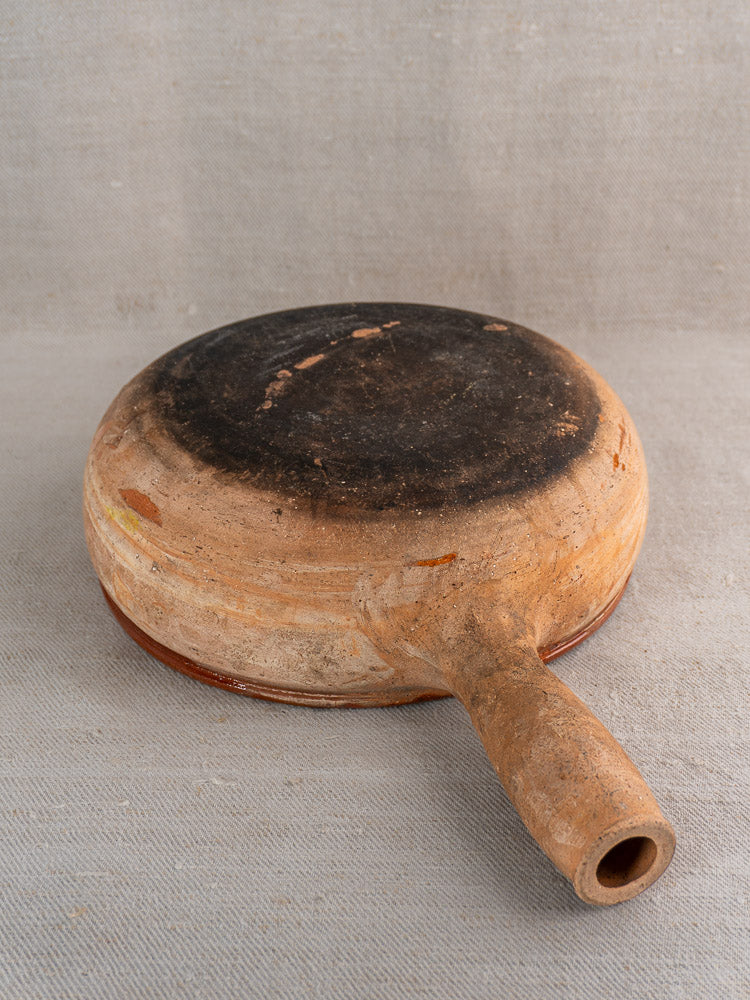 Vintage French Vallauris terracotta poêlon pan upside down, showing blackened base on beige fabric.
