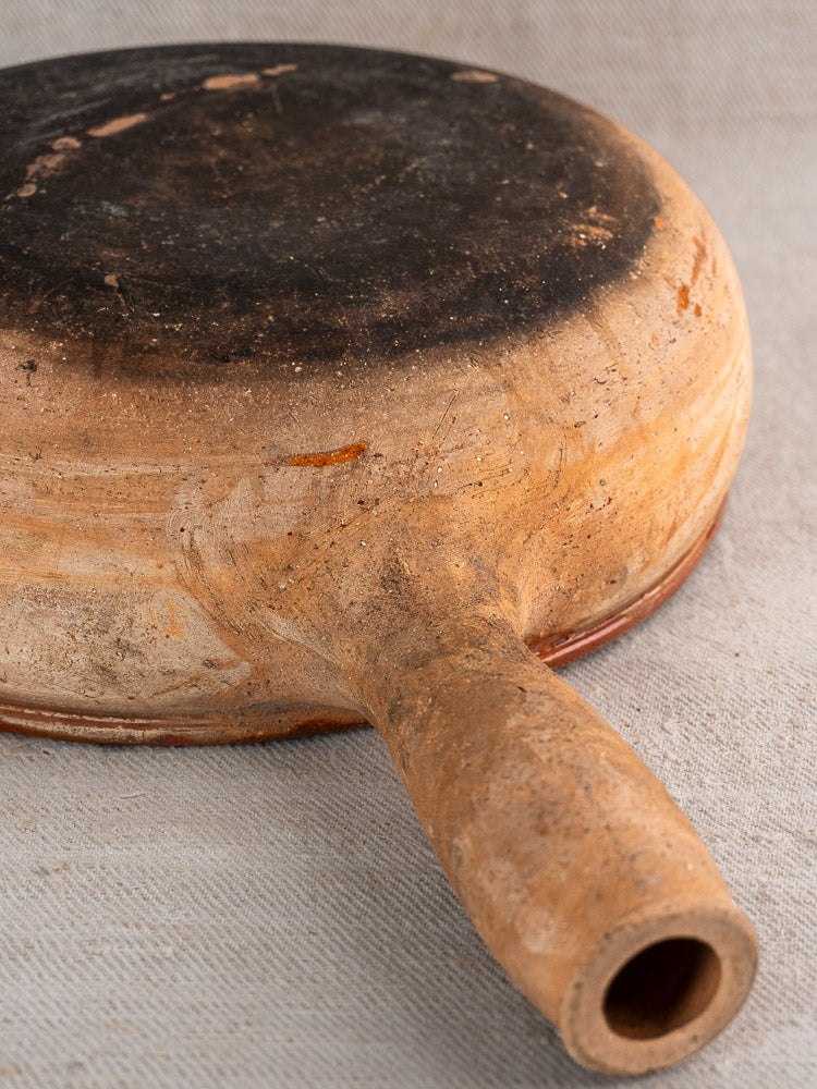 Underside of vintage French Vallauris terracotta poêlon with black scorch marks and textured surface.