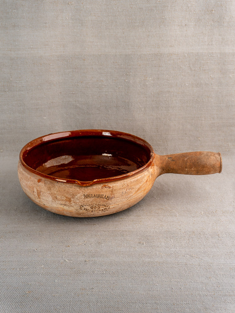 Vintage French Vallauris poêlon terracotta pan with glossy dark brown interior on gray fabric.
