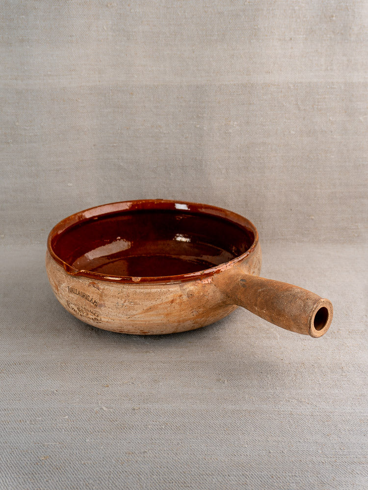 French Vallauris terracotta poêlon with deep brown glazed interior on textured gray fabric.