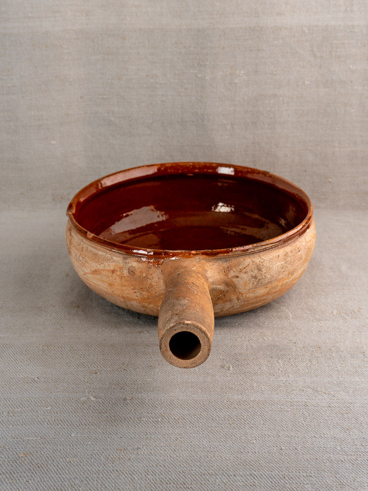 Vintage French Vallauris terracotta poêlon with single spout, glossy brown ceramic interior on gray fabric.