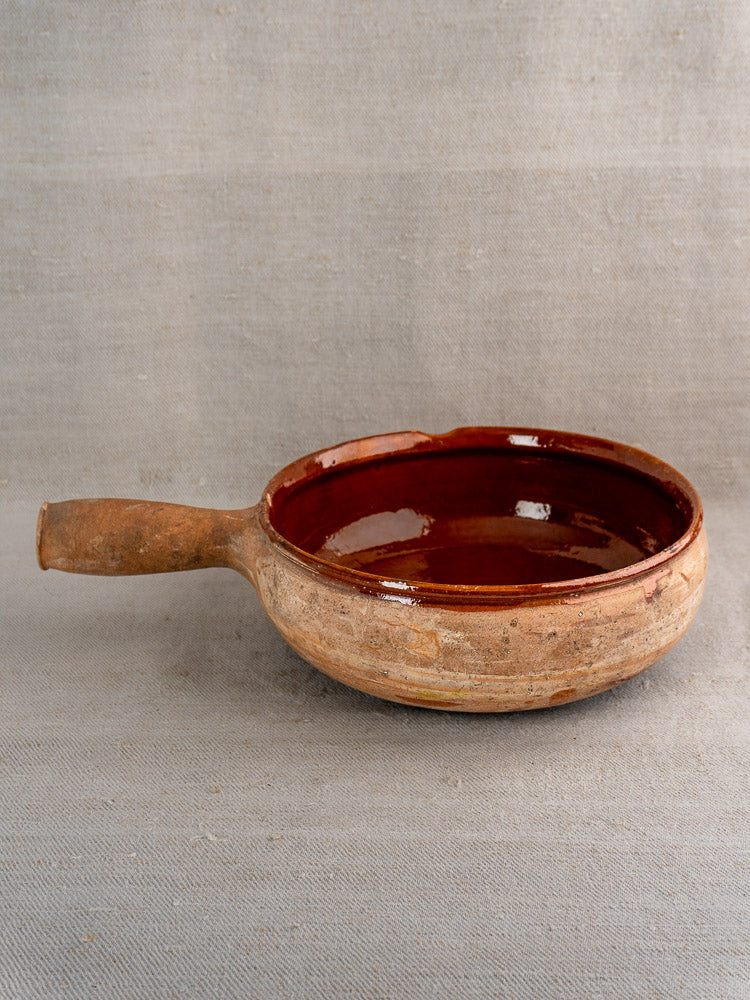 Vintage French Vallauris terracotta poêlon with handle and glossy reddish-brown interior on neutral surface.