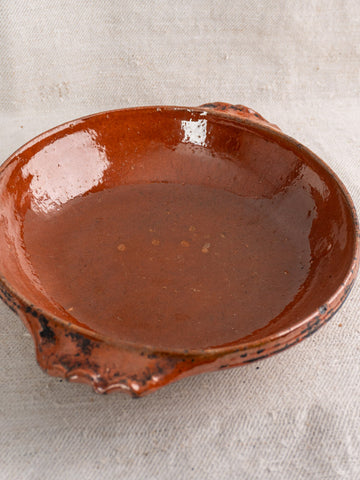 Mid-century Vallauris terracotta baking dish with handles and glossy finish, set on light textured fabric.
