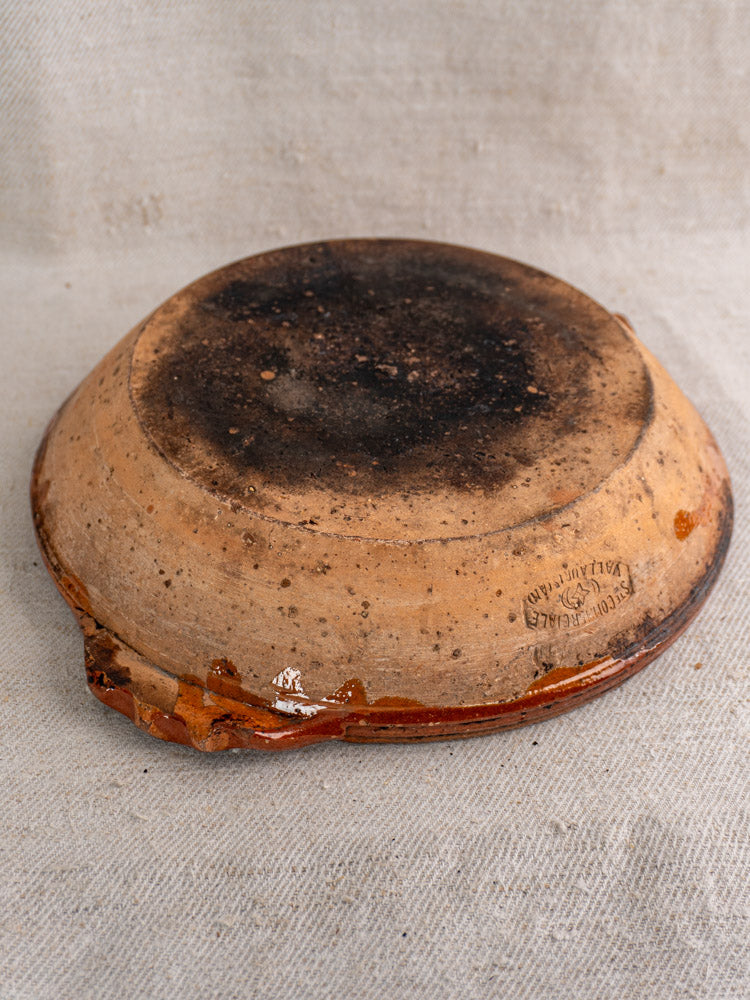 Mid-century Vallauris terracotta baking dish with handles, round form, stamped, on textured beige fabric.