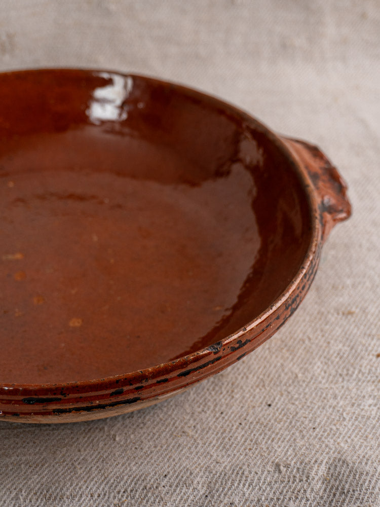 Rustic Mid-Century Vallauris terracotta baking dish with handles on textured beige fabric, vintage French kitchenware style.