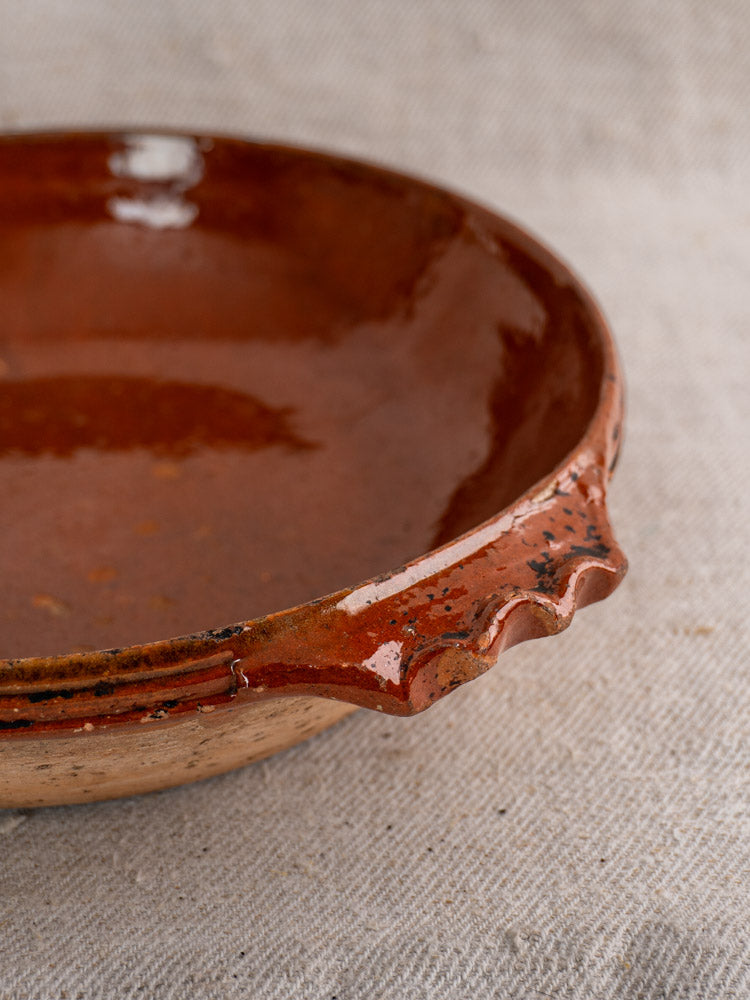 Rustic mid-century Vallauris terracotta baking dish with glazed finish and handles on textured beige fabric.