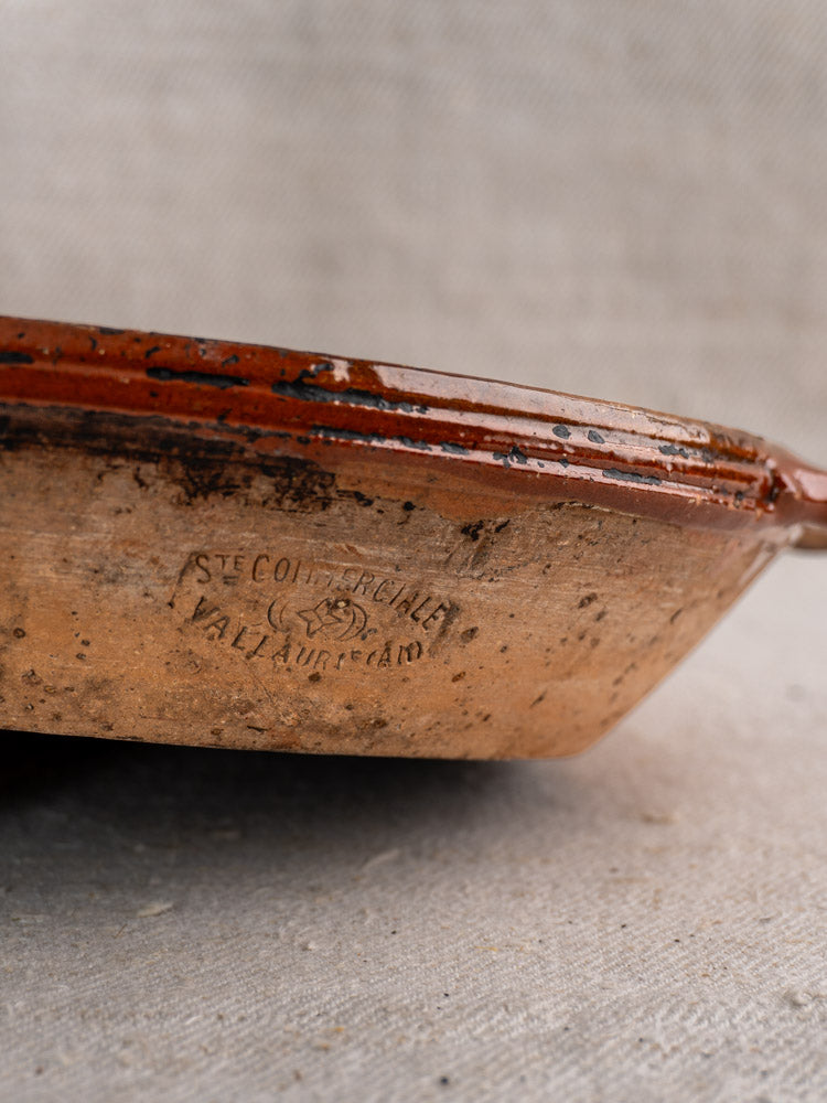 Mid-century Vallauris terracotta baking dish with handles, maker’s stamp, reddish-brown glazed rim, textured base.