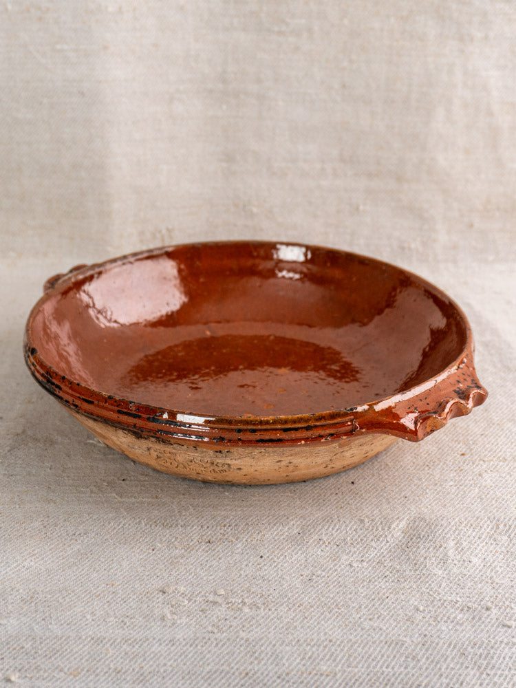 Mid-century Vallauris terracotta baking dish with handles and glossy finish, on light textured fabric background.