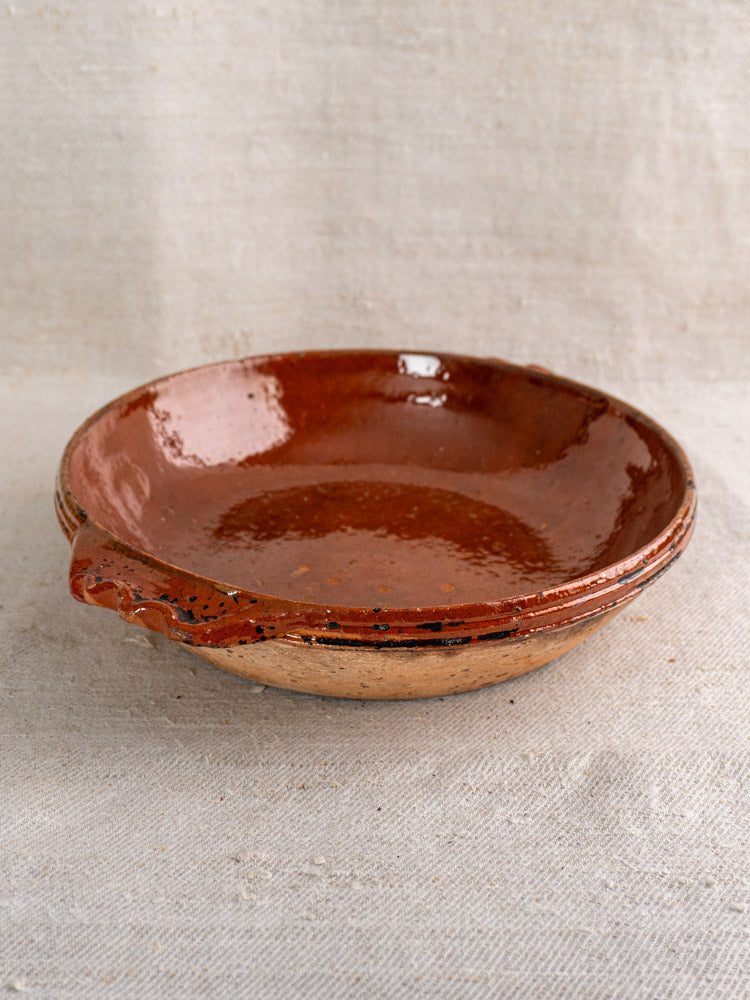Mid-century Vallauris terracotta baking dish with handles and glossy finish on neutral textured fabric background.