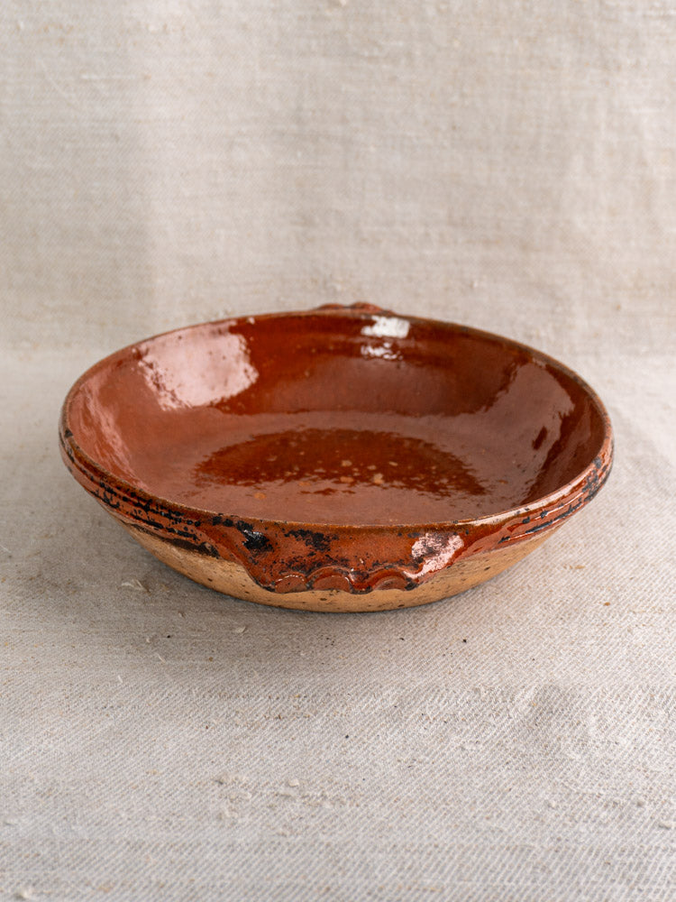 Mid-century Vallauris terracotta baking dish with handles, reddish-brown glazed interior, unglazed textured base on fabric.
