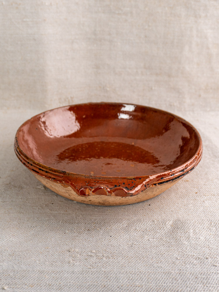 Mid-century Vallauris terracotta baking dish with handles and glossy finish on textured beige fabric background.