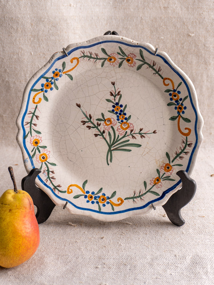 19th-century French faience plate with scalloped edge, hand-painted floral design and light crackling on beige background.
