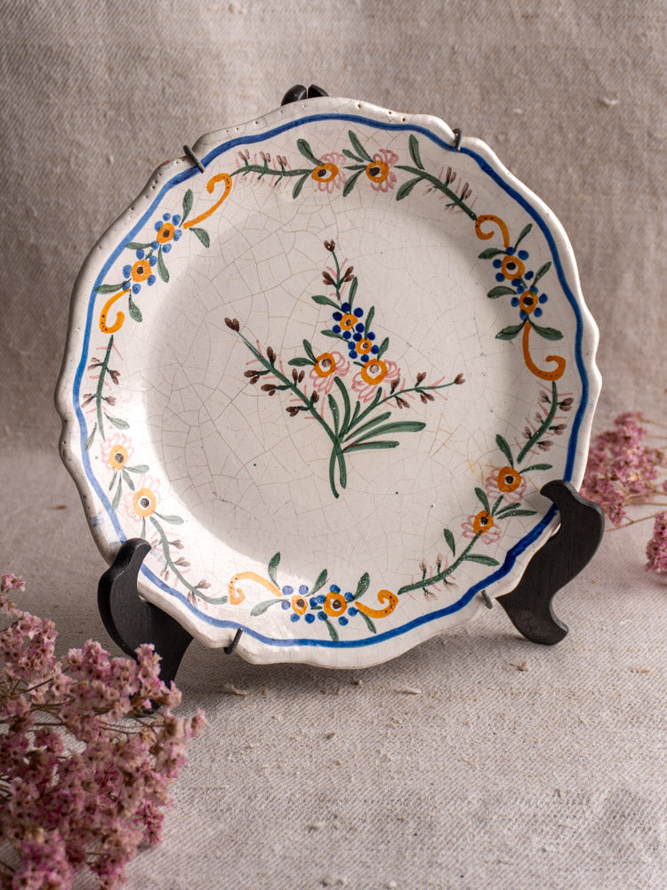 19th century French faience plate with scalloped edges and hand-painted florals on dark stand with pink dried flowers.