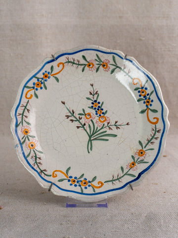 19th-century French faience plate with scalloped edge, hand-painted floral design and light crackling on beige background.