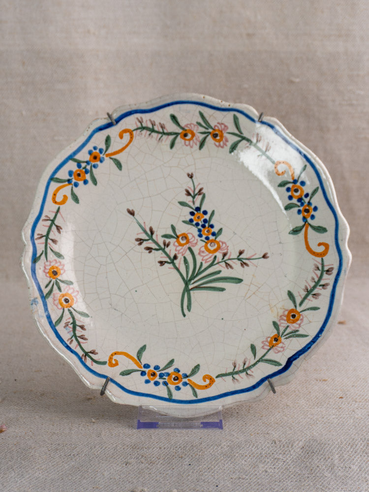 19th-century French faience plate with scalloped edge, hand-painted floral design and light crackling on beige background.