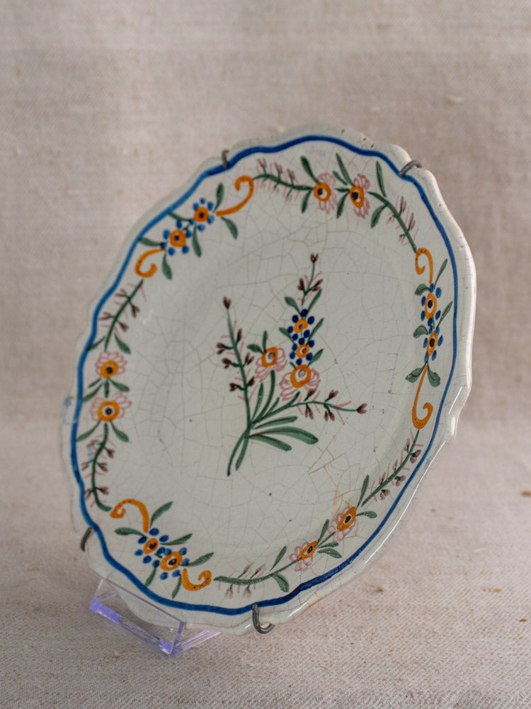 Antique French faience plate with scalloped edges, hand-painted orange, blue, and green florals on clear stand.