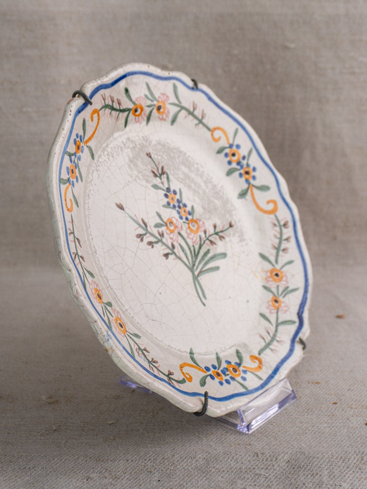 19th century French faience plate with scalloped edge, hand-painted blue, orange, and green floral design on display stand.