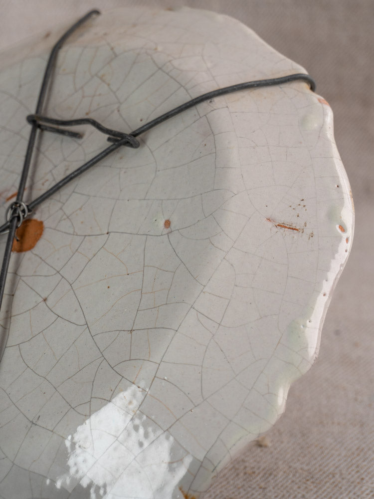 Antique French faience plate with hand-painted florals, off-white cracks, metal staples, and uneven edge.