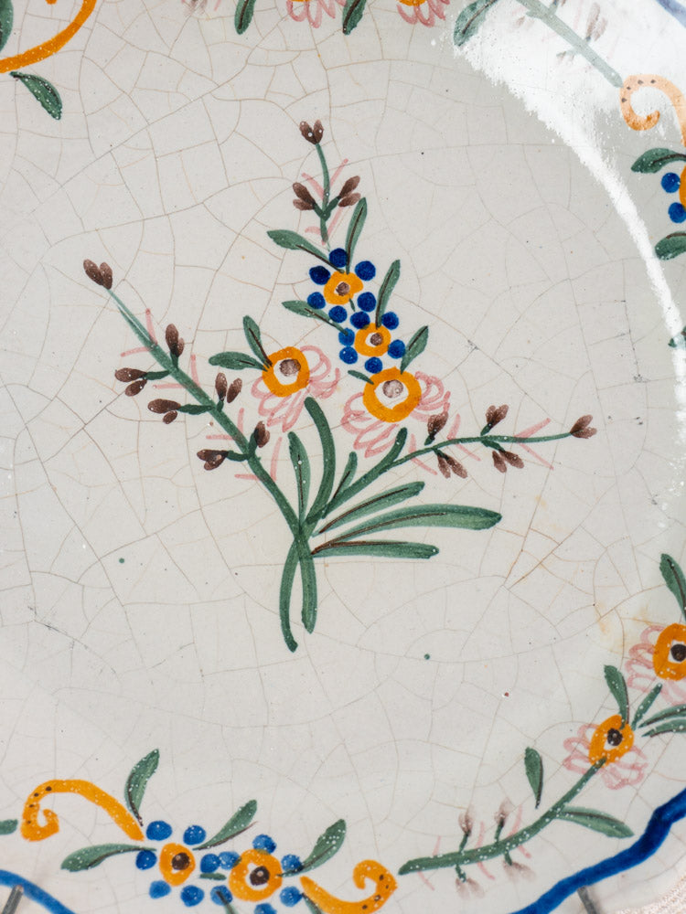Antique French faience plate with hand-painted green, blue, yellow, pink, and brown floral design, yellow-blue border.