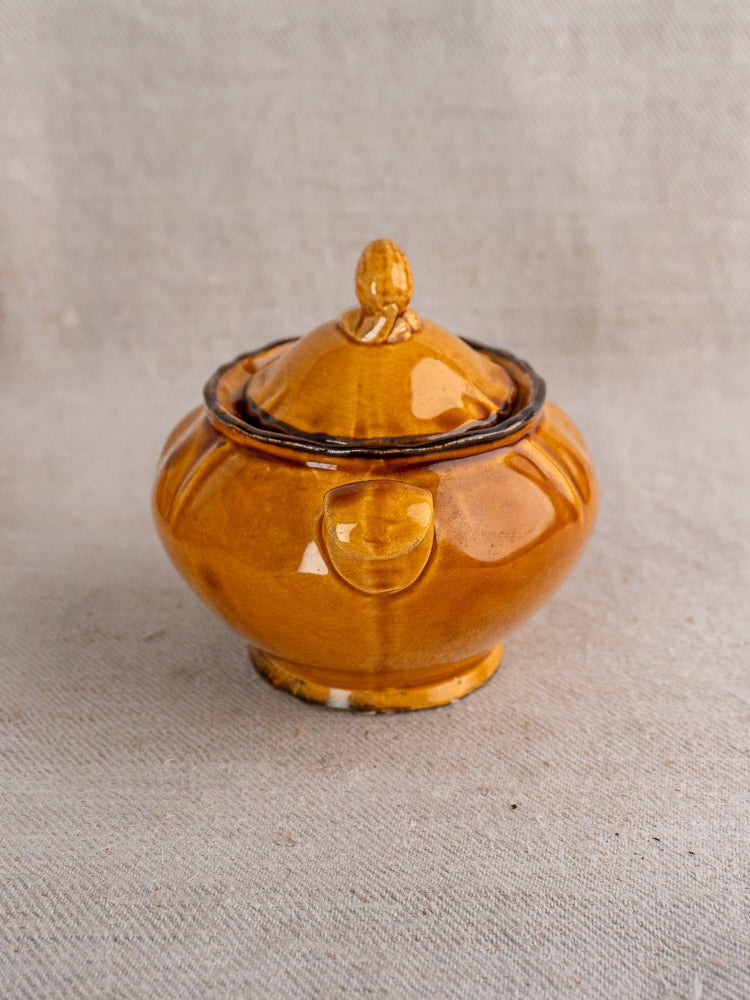 Small round earthenware demitasse pot with lid and shiny honey glaze on beige fabric.