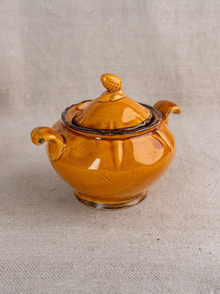 Glossy honey-glazed earthenware sugar bowl with acorn-shaped lid from French demitasse set on beige fabric.