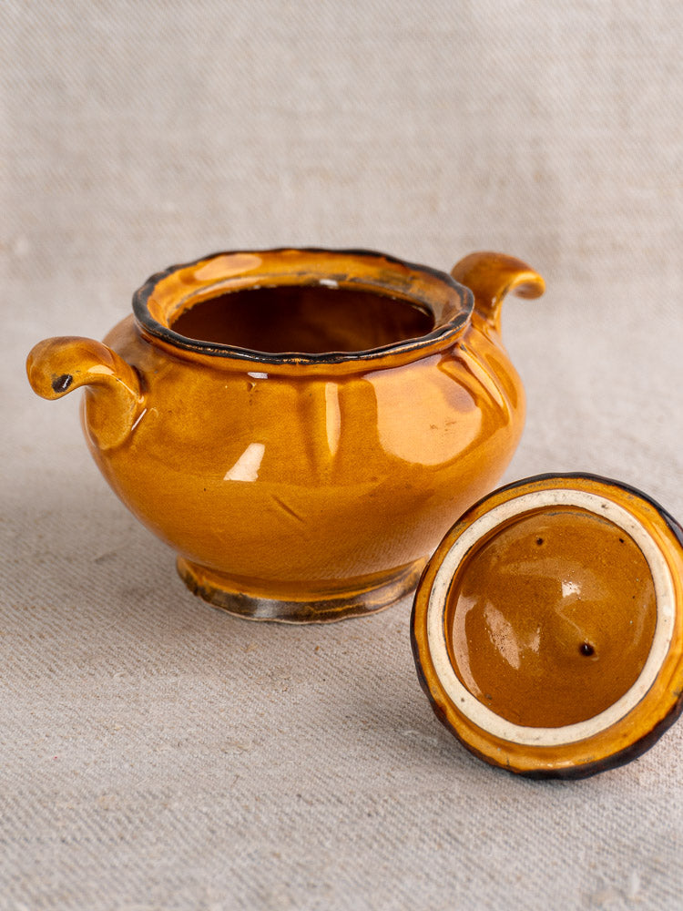 Yellow-brown vintage French earthenware demitasse pot with two handles and matching lid on beige surface.