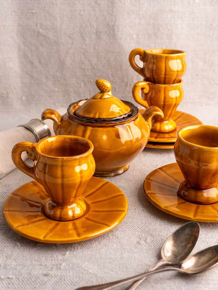 Honey-glazed French demitasse coffee set with teacups, saucers, lidded teapot, on neutral fabric.