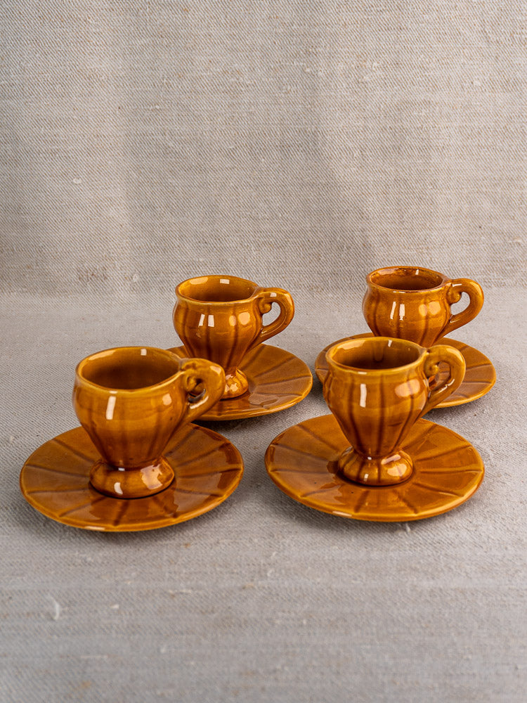 Set of four vintage French demitasse cups with saucers, honey amber glazed earthenware on neutral surface.