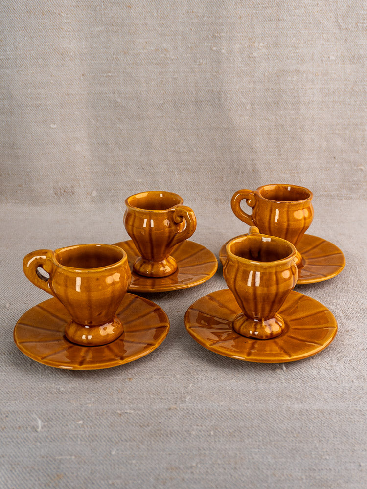 Vintage French earthenware demitasse coffee set with honey glaze, four cups and saucers on fabric.