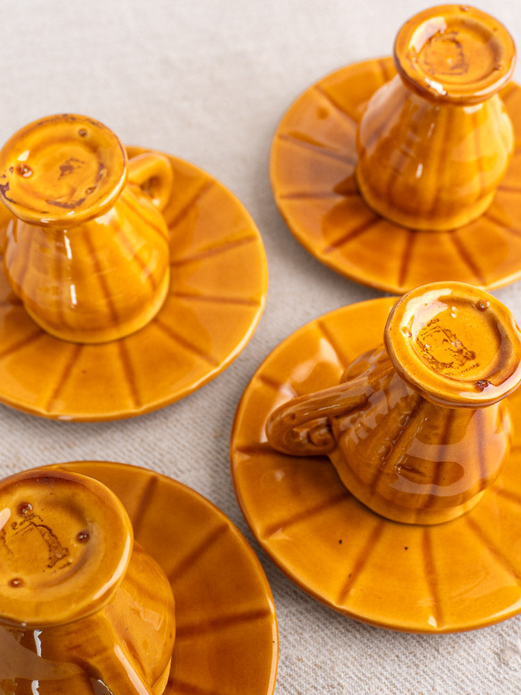 Amber earthenware demitasse cups with glossy honey glaze and radial patterns, on saucers.