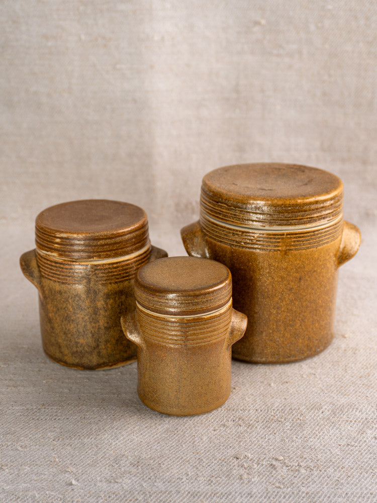 Set of five French Digoin Grespots stoneware pots with lids on beige fabric background.