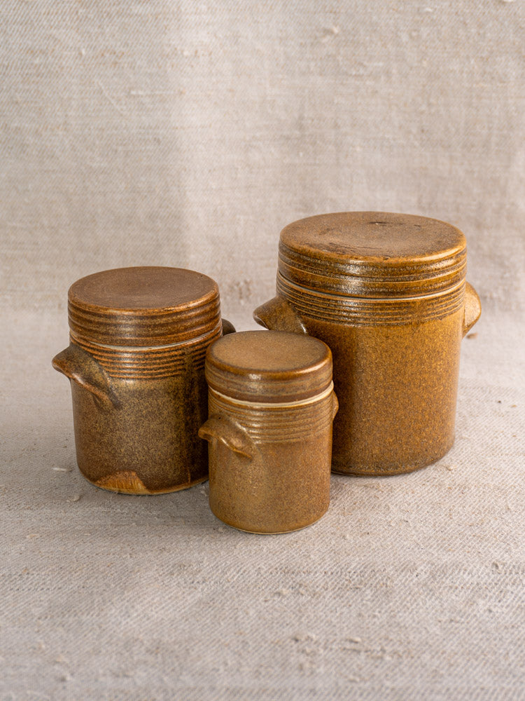 Set of five graduated vintage French Digoin Grespots stoneware pots with lids on beige fabric.