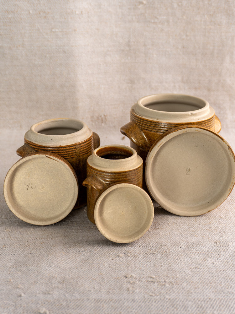 Set of five vintage French Digoin Grespots stoneware pots on textured beige fabric background.