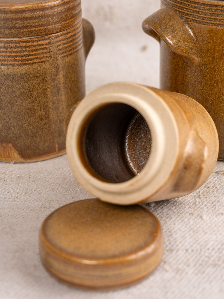 Small French Digoin stoneware pot with lid off, two matching pots behind on beige fabric.