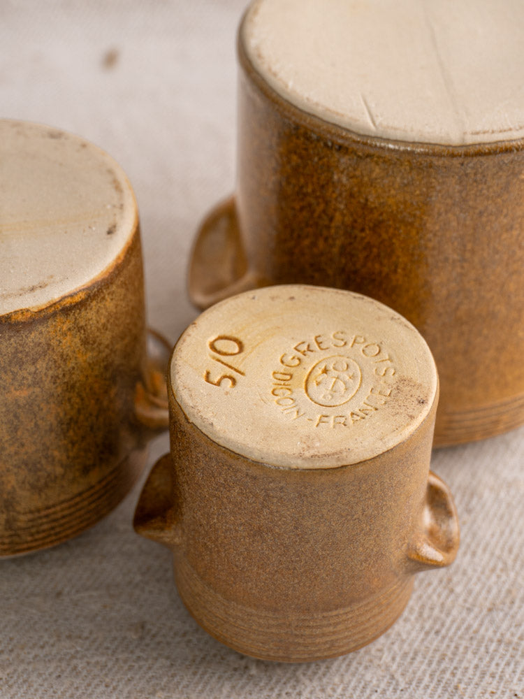 Three small brown Digoin Grespots French stoneware pots, stamped bases, on textured fabric.