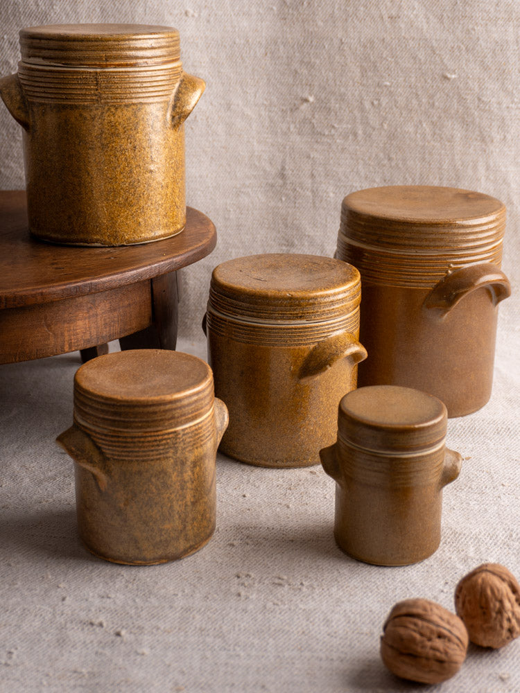 Set of five vintage French Digoin Grespots stoneware pots with lids on textured beige surface.