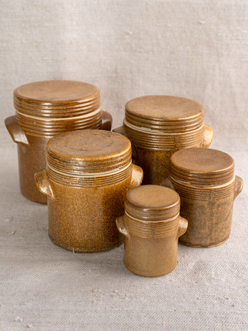 Set of five vintage French Digoin Grespots stoneware pots with ribbed lids and side handles, on light fabric.