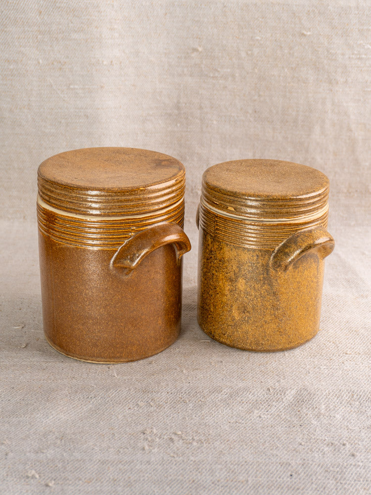 Pair of vintage French Digoin Grespots stoneware pots with lids and side handles on beige fabric.