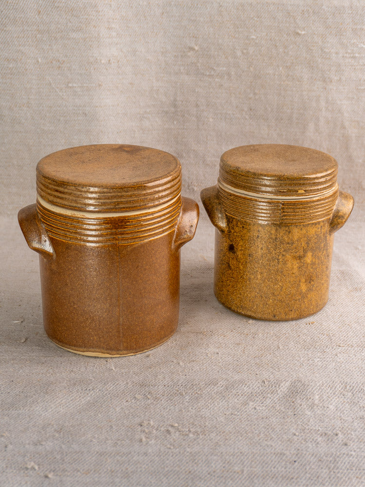 Pair of vintage French Digoin Grespots stoneware pots with lids and small handles on beige fabric.
