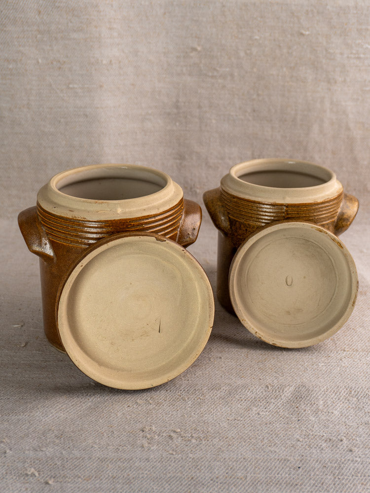 Set of vintage French Digoin Grespots stoneware pots with handles and lids on beige fabric.