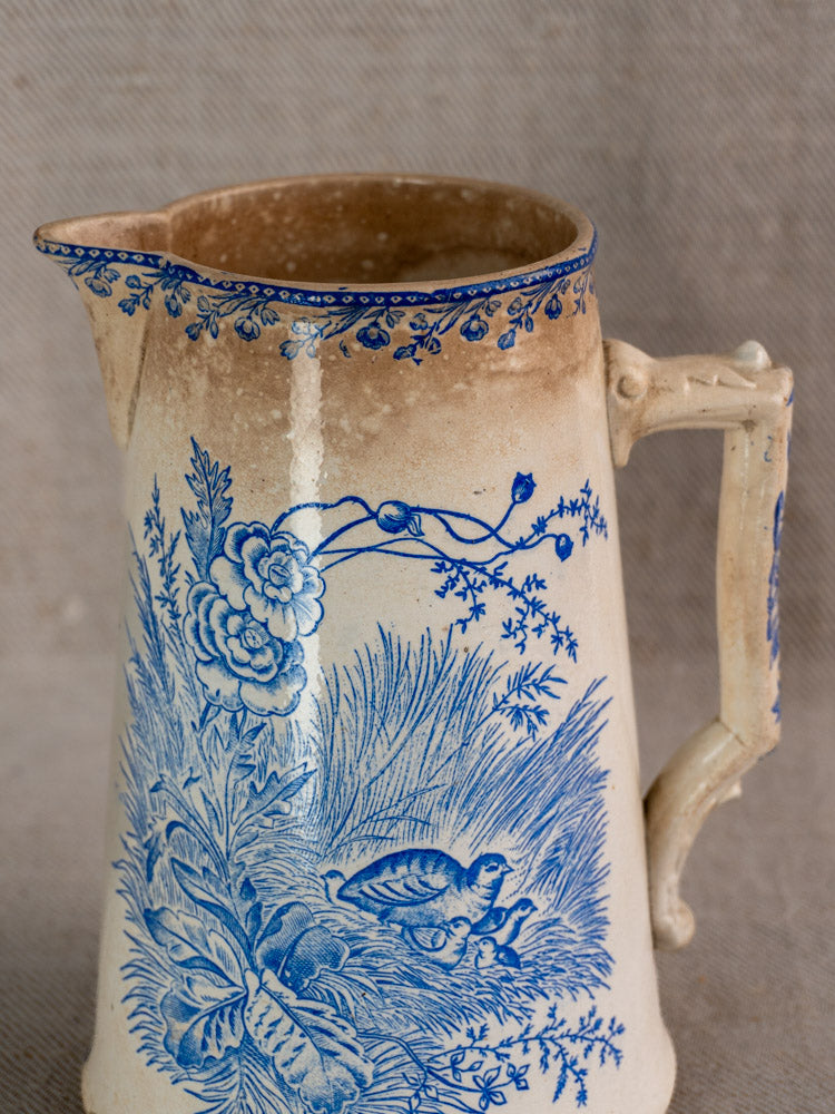 Antique French Fenal Frères ceramic pitcher with blue Oiseaux motifs and ornate handle on gray background.