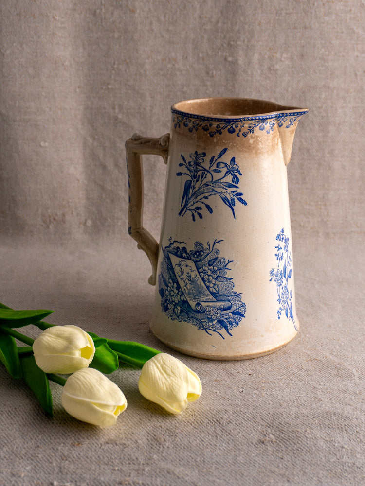 Antique French Fenal Frères Pichet with Pexonne Oiseaux pattern beside three white tulips on beige fabric.
