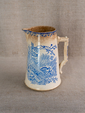 Antique French Fenal Frères Pichet with blue floral motif and ornate handle on beige fabric.