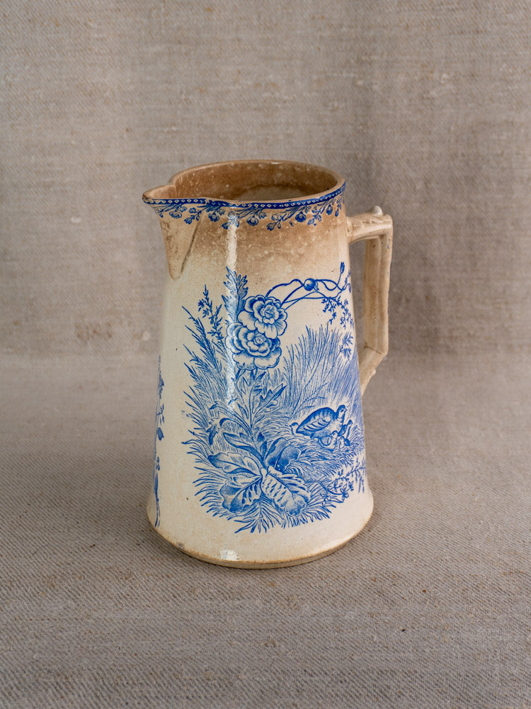 Antique French Fenal Frères Pichet, cream ceramic with blue floral Pexonne Oiseaux pattern, on beige fabric.