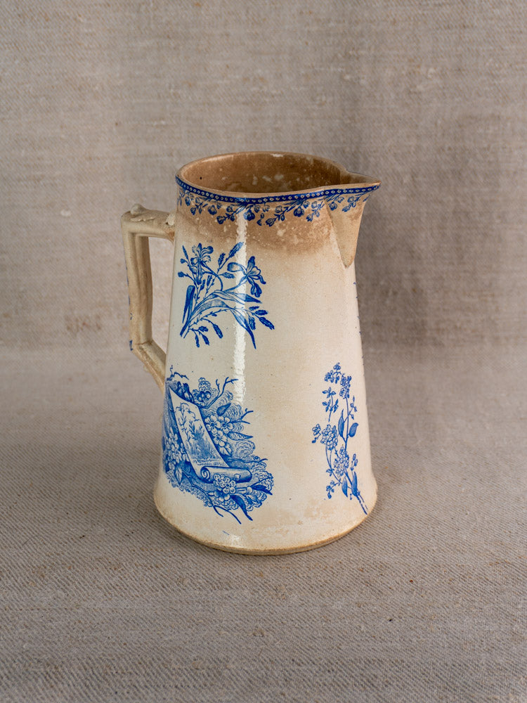 Antique French Fenal Frères ceramic pitcher with blue floral Pexonne Oiseaux pattern on beige fabric.