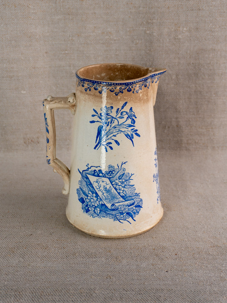 Antique French Fenal Frères ceramic pichet with blue floral motifs, Pexonne Oiseaux pattern, on beige fabric.